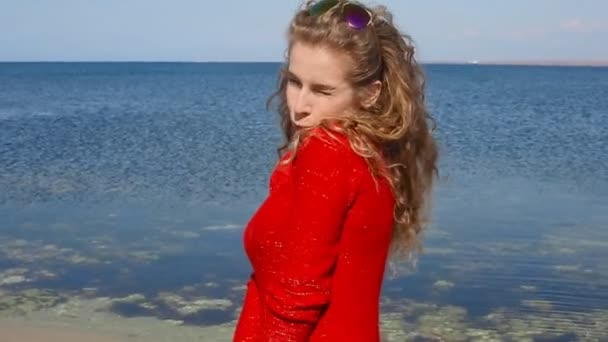 Close-up portret van vrouw lopen hand door krullend haar waait in de wind van zee op strand. Gelukkige vrouw over blauwe hemel. — Stockvideo