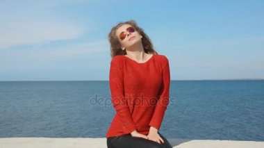 Kadın moda trendy güneş gözlüğü çalışan el sahilde deniz rüzgarda üfleme kıvırcık saçlarının arasından portresi kapatın. Mavi gökyüzü üzerinde mutlu erkek