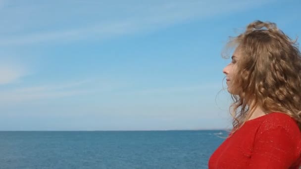 Close up portrait of woman running hand through curly hair blowing in wind by sea on beach. Happy female over blue sky. — Stock Video