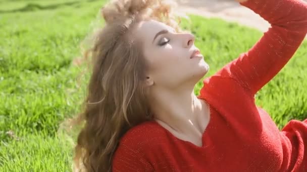 Heureuse femme souriante allongée sur de l'herbe verte profitant de la vie, jeune femme s'amusant à l'extérieur dans un parc de printemps . — Video