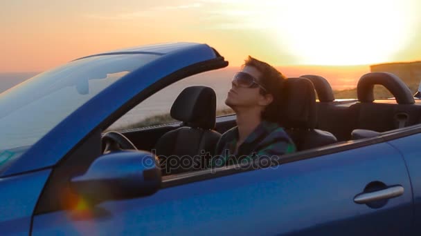 Close-up portret van jonge man ontspannen in cabriolet, op het strand boven de zee. Knappe jongen bij zonsondergang — Stockvideo