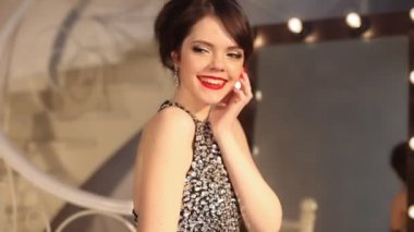 Makyaj ve saç modeli, kırmızı manikür çivi ve küpe takı ile gülümseyen kız mutlu. Ayna, soyunma odasında poz içinde makyaj için ampuller ile tarafından poz şık elbiseli çekici genç esmer