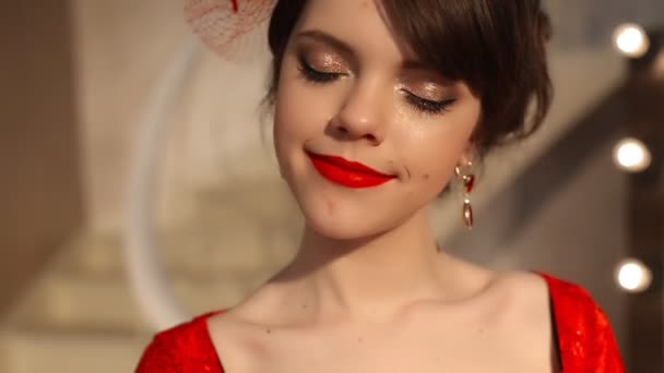 Nahaufnahme der schönen Mode junge Mädchen in Retro-Hut und rotem Kleid, brünettes Modell mit roten Lippen Make-up, elegante Frisur, Anhänger Frauen setzen Schmuck posiert durch Spiegel mit Glühbirnen für Make-up in Dressing — Stockvideo