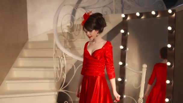 Крупним планом красива молода дівчина моди в ретро капелюсі і червоній сукні, брюнетка модель з червоними губами макіяж, елегантна зачіска, підвісні жінки набір прикрас позує дзеркало з цибулинами для макіяжу в одязі — стокове відео