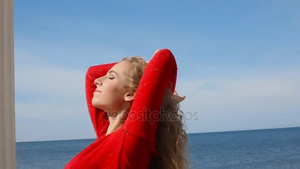 Close up portrait of woman running hand through curly hair blowing in wind by sea on beach. Happy female over blue sky. — Stock Video