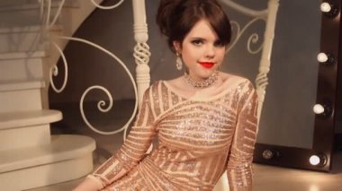 Mutlu genç gülümseyen kız makyaj ve saç modeli ile kırmızı tırnakları manikürlü. Payet çekici genç esmer elbise kameraya poz modern oda katta oturan.