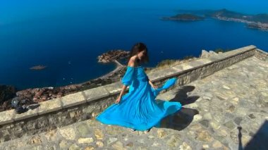 Sağlıklı uzun saçlı kız elbise üfleme gülümseyen güzel esmer. Mutlu genç kadın zevk ve having Fun üzerinde deniz ve mavi gökyüzü. Sveti Stefan, Karadağ.