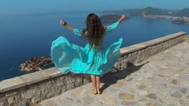 Sağlıklı uzun saçlı kız elbise üfleme gülümseyen güzel esmer. Mutlu genç kadın zevk doğa ve deniz ve mavi gökyüzü Eğleniyor. Sveti Stefan, Karadağ.