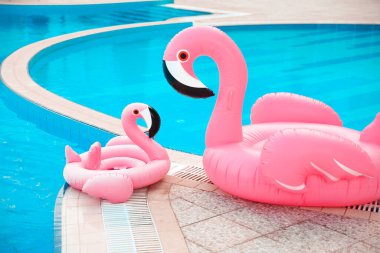Aile görünüşü. Mavi sularda iki pembe havuz flamingo yüzer, havuz partisi oyuncağı. Devasa Şişirilebilir Yüzme Halkası. Yaz tatili lüks tatil beldesi. 