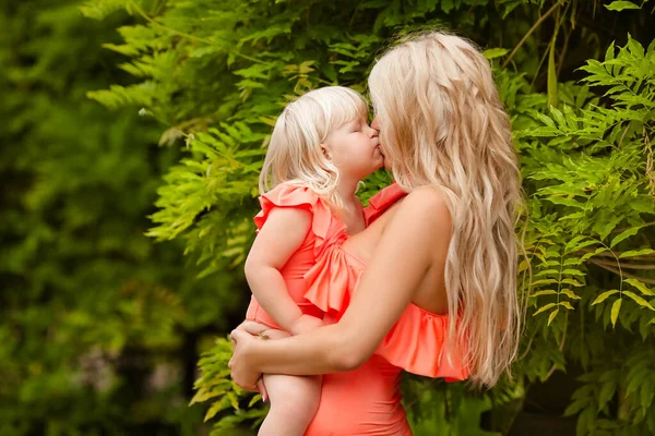 家族みたいに 美しい母は緑の公園の上に彼女の小さなブロンドの娘を持っています 夏休みに かわいい女の子は楽しみを持っているファッションオレンジ水着で身に着けています 親の屋外肖像画 — ストック写真