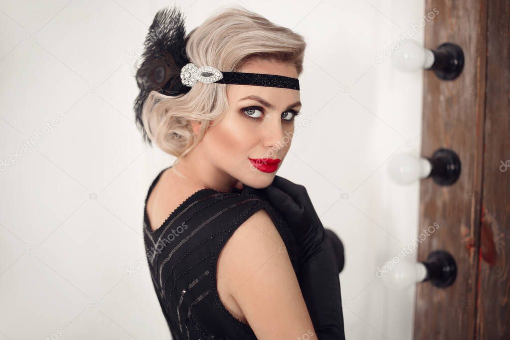 Blonde wavy hairstyle. Elegant woman portrait in retro style. Beautiful girl wears in vintage black dress and gloves. Hollywood red lips makeup. 