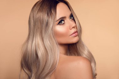 Sarışın, dalgalı saç stili. Güzel, moda sarışın kadın portresi. Makyajlı güzel bir manken, uzun sağlıklı saç stili stüdyo bej arka planında izole edilmiş..