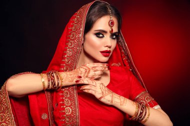Kızıl gelinlik giymiş güzel Hintli bir kızın portresi. Kundan mücevher seti olan genç Hindu kadın model. Geleneksel Hint kostümü lehenga choli. Kına resmi, gelinin ellerinde mehendi..