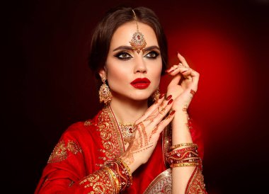Kızıl gelinlik giymiş güzel Hintli bir kızın portresi. Kundan mücevher seti olan genç Hindu kadın model. Geleneksel Hint kostümü lehenga choli. Kına resmi, gelinin ellerinde mehendi..