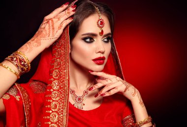 Kızıl gelinlik giymiş güzel Hintli bir kızın portresi. Kundan mücevher seti olan genç Hindu kadın model. Geleneksel Hint kostümü lehenga choli. Kına resmi, gelinin ellerinde mehendi..