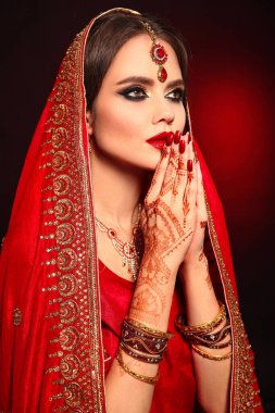 Kızıl gelinlik giymiş güzel Hintli bir kızın portresi. Kundan mücevher seti olan genç Hindu kadın model. Geleneksel Hint kostümü lehenga choli. Kına resmi, gelinin ellerinde mehendi..