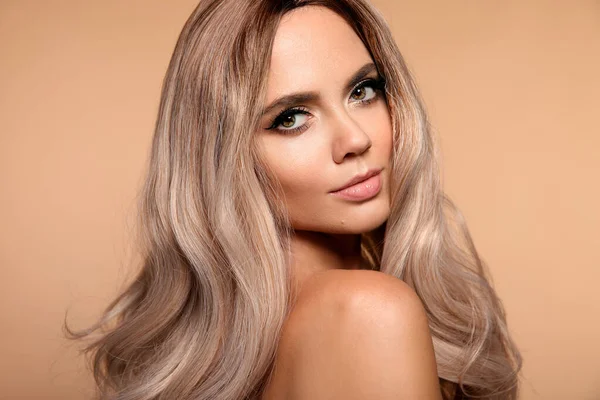 Sarışın, dalgalı saç stili. Güzel, moda sarışın kadın portresi. Makyajlı güzel bir manken, uzun sağlıklı saç stili stüdyo bej arka planında izole edilmiş..