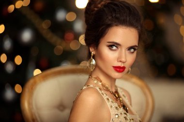 Düğün saç stili olan zarif bir kadının Noel portresi. Güzellik makyajı. Balo elbisesi içinde güzel esmer kız. Bokeh ışıkları üzerinde modern sandalyede oturuyor. Noel süslemeleri..