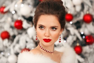 Zarif kadın Cristmas portresi. Yakut mücevher seti ve düğün saç stili olan güzel esmer kadın Noel ağacı arka planında poz veren güzellik makyajı yapıyor.