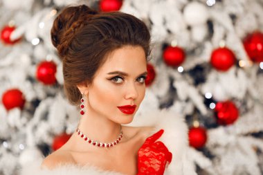 Yakut mücevher seti ve kırmızı eldivenli zarif bir kadının gelin portresi. Düğün saç stili olan güzel esmer kadın, makyaj malzemesi Noel ağacı arka planında poz veriyor.