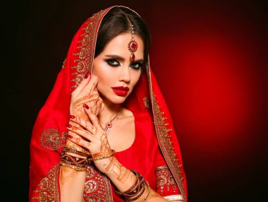 Kızıl gelinlik giymiş güzel Hintli bir kızın portresi. Kundan mücevher seti olan genç Hindu kadın model. Geleneksel Hint kostümü lehenga choli. Kına resmi, gelinin ellerinde mehendi..