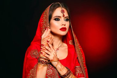 Kızıl gelinlik giymiş güzel Hintli bir kızın portresi. Kundan mücevher seti olan genç Hindu kadın model. Geleneksel Hint kostümü lehenga choli. Kına resmi, gelinin ellerinde mehendi..