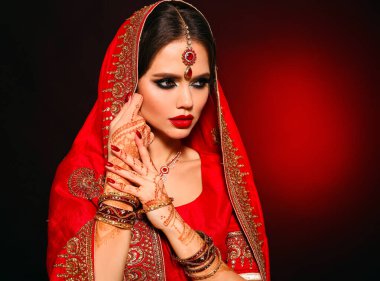 Kızıl gelinlik giymiş güzel Hintli bir kızın portresi. Kundan mücevher seti olan genç Hindu kadın model. Geleneksel Hint kostümü lehenga choli. Kına resmi, gelinin ellerinde mehendi..