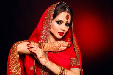 Kızıl gelinlik giymiş güzel Hintli bir kızın portresi. Kundan mücevher seti olan genç Hindu kadın model. Geleneksel Hint kostümü lehenga choli. Kına resmi, gelinin ellerinde mehendi..
