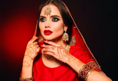 Kızıl gelinlik giymiş güzel Hintli bir kızın portresi. Kundan mücevher seti olan genç Hindu kadın model. Geleneksel Hint kostümü lehenga choli. Kına resmi, gelinin ellerinde mehendi..