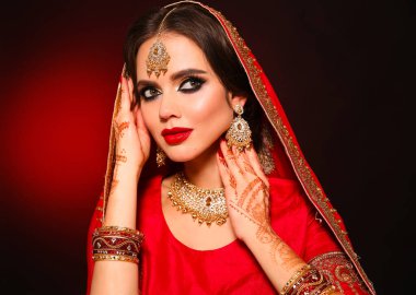 Kızıl gelinlik giymiş güzel Hintli bir kızın portresi. Kundan mücevher seti olan genç Hindu kadın model. Geleneksel Hint kostümü lehenga choli. Kına resmi, gelinin ellerinde mehendi..