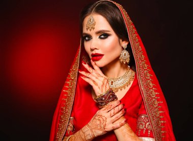 Kızıl gelinlik giymiş güzel Hintli bir kızın portresi. Kundan mücevher seti olan genç Hindu kadın model. Geleneksel Hint kostümü lehenga choli. Kına resmi, gelinin ellerinde mehendi..