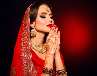 Kızıl gelinlik giymiş güzel Hintli bir kızın portresi. Kundan mücevher seti olan genç Hindu kadın model. Geleneksel Hint kostümü lehenga choli. Kına resmi, gelinin ellerinde mehendi..