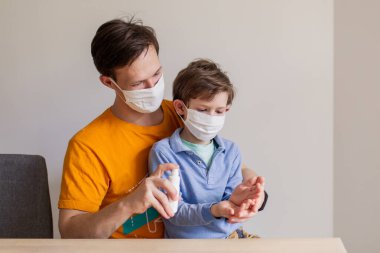 El dezenfeksiyonu ve antiseptik. Koronavirüs covid-19 virüsünün yüzeylerinin antibakteriyel spreyi. Baba oğluna hijyen öğretiyor. Tıbbi maskeli insanlar. Pandemik koruma