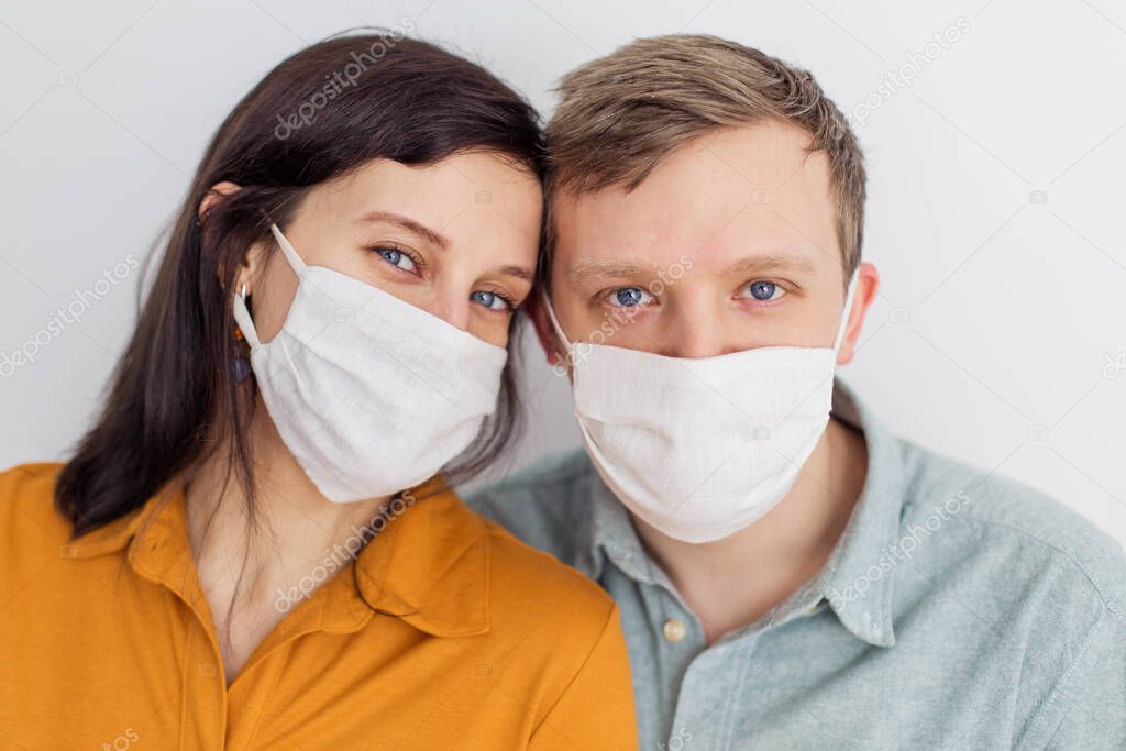 Faces of people in protective masks from coronavirus hand made. A beautiful blue-eyed quarantined couple protecting themselves from a pandemic. Positive young youth. Lifestyle COVID-19 home together