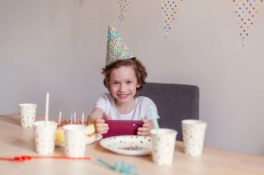 Çocuk çevrimiçi doğum gününü kutluyor. Videokonferans bayramı tebrikleri. Pasta süslemesi. Sosyal mesafeli izolasyon evde kalır. Video arama cep telefonu aleti. Erkek çocuk Avrupalı yalnız bekar