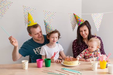İki çocuklu mutlu bir aile doğum gününü kutlar. Kekle birlikte. Anne, baba, oğul, kardeş. Bir parti. Genç aile bir arada. Ebeveynlik modern bir şey. Bayram mumlarını üfle. Bir dilek tut.