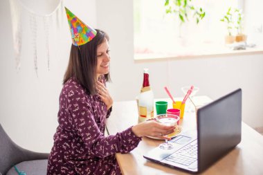 Genç bir kadın doğum gününü internette alkol içerek kutluyor. Video konferans dizüstü bilgisayarı parti interneti. Alkolizm yeni teknoloji karantinası sosyal izolasyon. Boş zaman. Görüntülü konuşma arkadaşlar tebrikler.