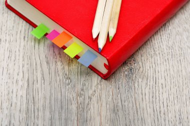Kırmızı günlük defter ve Resepsiyon ahşap doku üzerinde renkli kalemler.