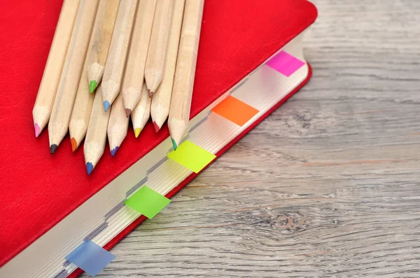 Cuaderno diario rojo y lápices de colores en la textura de madera del escritorio . — Foto de Stock