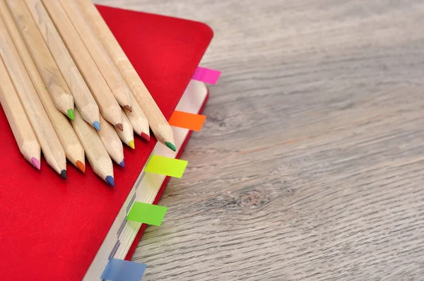 Cuaderno diario rojo y lápices de colores en la textura de madera del escritorio . — Foto de Stock
