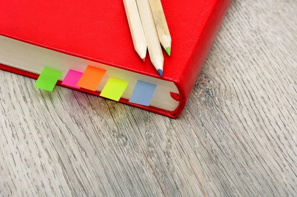 Kırmızı günlük defter ve Resepsiyon ahşap doku üzerinde renkli kalemler.
