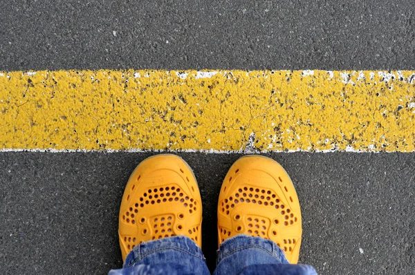 Bovenaanzicht van gele schoenen op het asfaltweg met gele lijn — Stockfoto