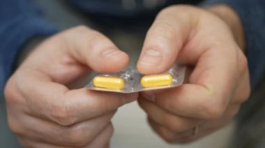 Erkek eli su toplayan torbalardan hap alır. Erkek eli kapalı beyaz turuncu yuvarlak tablet dökün. Elinde tıbbi doz hapı var. Grip, yetişkin, soğuk algınlığı, hastalık, virüs, ağır çekim hapları..