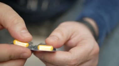 Erkek eli su toplayan torbalardan hap alır. Erkek eli kapalı beyaz turuncu yuvarlak tablet dökün. Elinde tıbbi doz hapı var. Grip, yetişkin, soğuk algınlığı, hastalık, virüs, ağır çekim hapları..