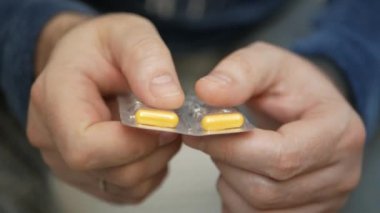 Erkek eli su toplayan torbalardan hap alır. Erkek eli kapalı beyaz turuncu yuvarlak tablet dökün. Elinde tıbbi doz hapı var. Grip, yetişkin, soğuk algınlığı, hastalık, virüs, ağır çekim hapları..