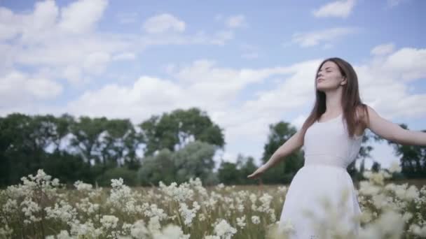 Молодая красивая женщина посреди цветочного луга с распростертыми руками — стоковое видео