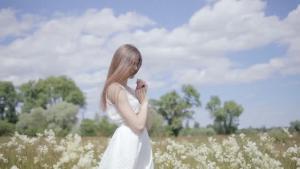 Giovane bella donna in mezzo al prato fiorito, guardando in basso, vento nei capelli — Video Stock