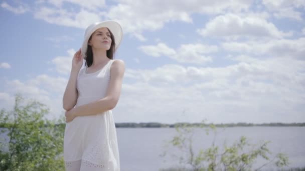 Gökyüzü bulutlar ve dolu ile suya yakın genç güzel kadın — Stok video