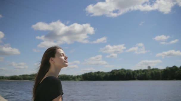 Jovem mulher bonita sentada perto do rio com os olhos fechados — Vídeo de Stock