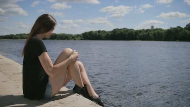 Mladá krásná žena sedící poblíž řeky při pohledu na řece — Stock video